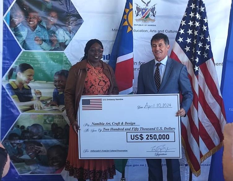 US-Botschafter Randy Berry (rechts) übergibt einen symbolischen Scheck an Vize-Kulturministerin Faustina Caley; © Hitradio Namibia